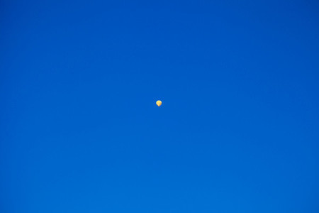 Yellow hot air balloon flying very high in the blue sky