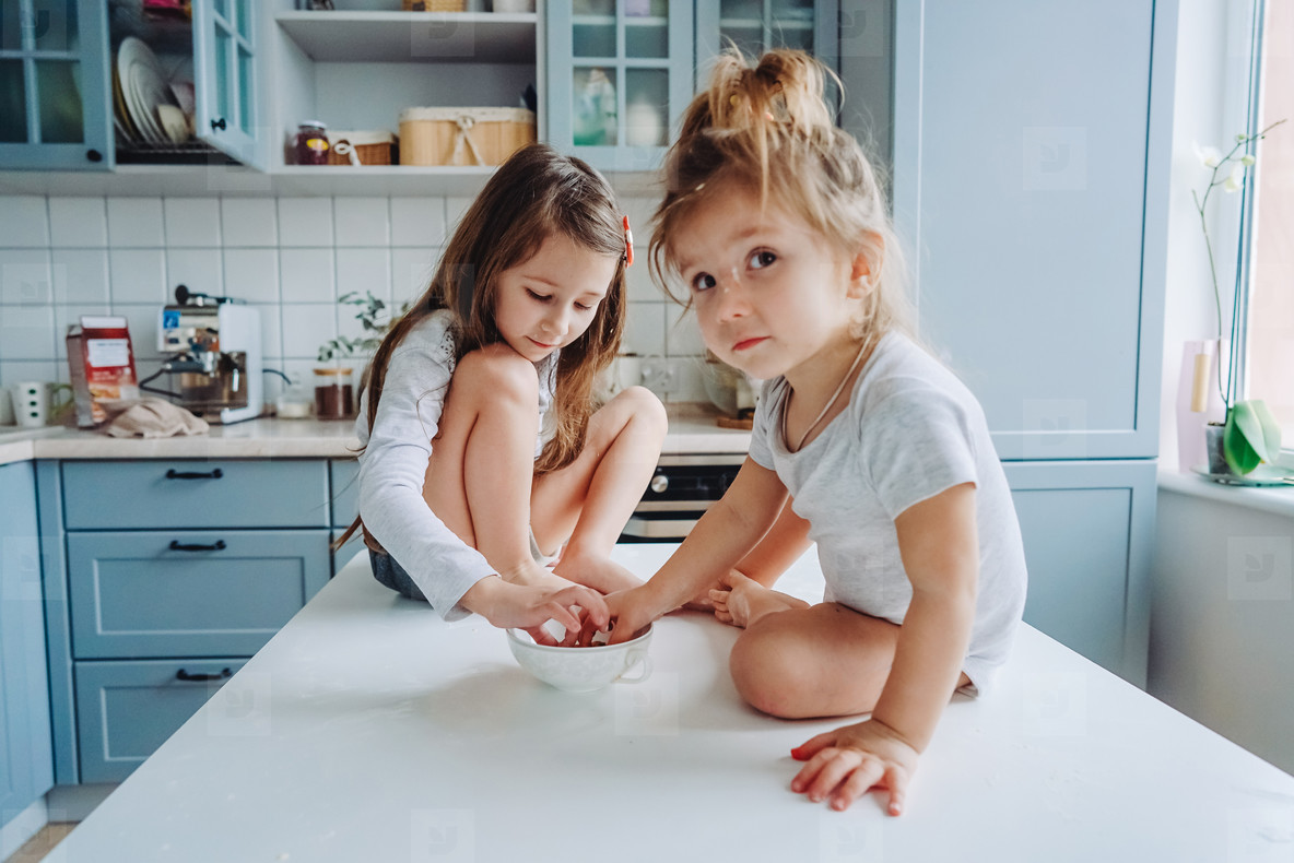 Two little girls in the kitchen sitting on the table