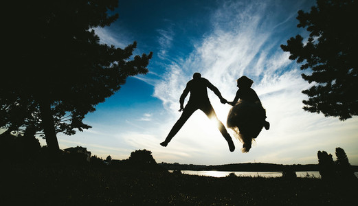 groom and bride jumping against the beautiful sky