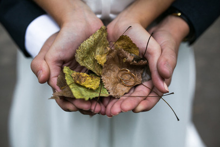 Bride and groom holding wedding rings and autumn leaves in hands