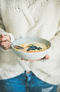 Woman in jeans and sweater eating oatmeal porriage with berries