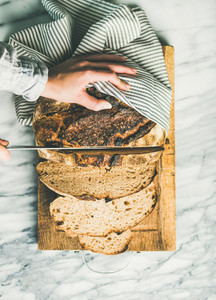Female hands cutting freshly baked sourdough bread  vertical composition