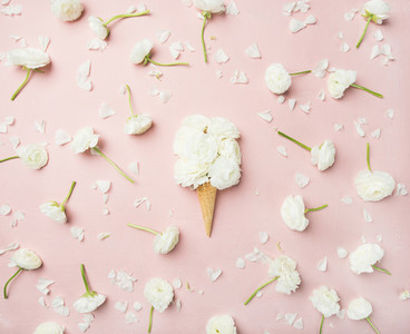 Waffle cone with white buttercup flowers over light pink background
