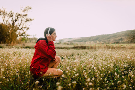 Girl listening to music with headphones sitting among wildflowers