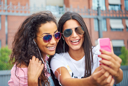 Two young girlfriends smiling and taking selfies together outside