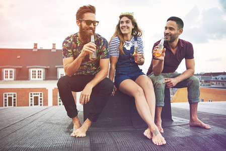 Happy group of three barefoot adults drinking beer