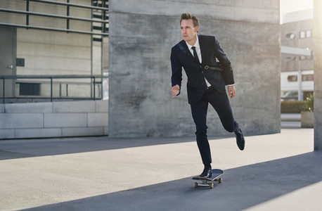 Confident successful man in suit riding skateboard