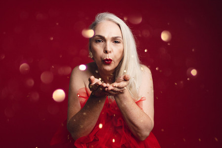 Attractive senior woman blowing glitters