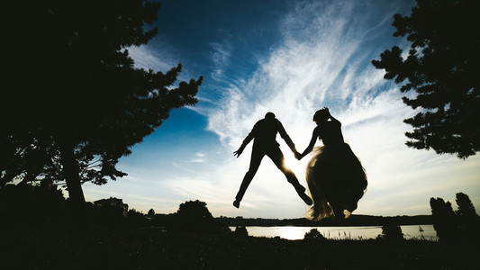 groom and bride jumping against the beautiful sky