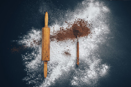 wooden rolling pin with flour and a spoon of cocoa on a black and blue background Concept creative chaos