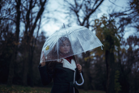 girl holding a transparent umbrella in an autumn park and looking at a fallen leaf  Concept Autumn after Rain