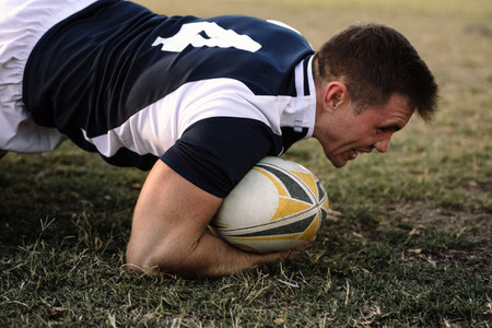 Strong rugby player with ball on ground