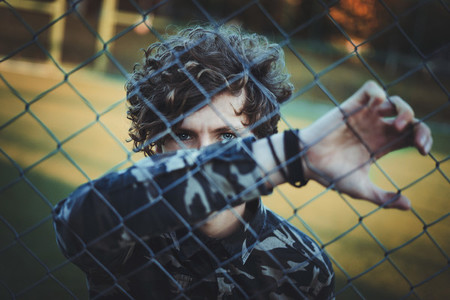 curly haired boy in camouflage shirt hiding his face with his hand behind the net