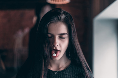 The girl close her eyes and hold a tablet on tongue