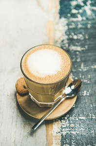 Classic foamy cappuccino coffee in glass over wooden background