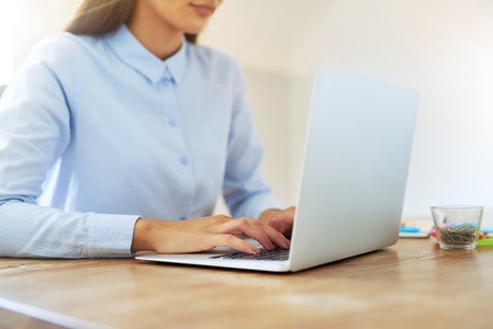 Hands of partially obscured woman typing on laptop