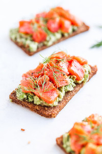 Close up view of three sandwiches with rye bread  avocado and smoked salmon on a white kitchen table