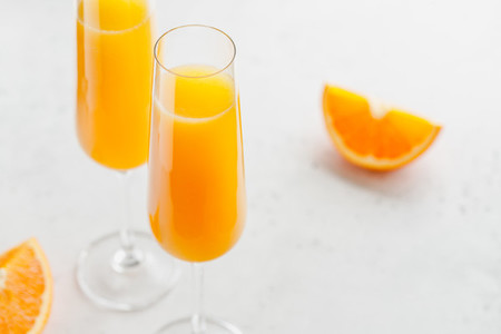 Brunch Mimosa classic cocktail is made from orange juice and sparkling wine or Champagne in flute glasses on a grey table