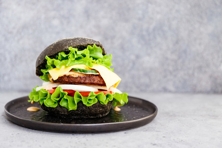 Black burger with marble beef patty  cheese and fresh vegetables served on a black plat  Copy space