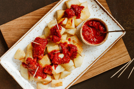 Top view on traditional tapas of Spanish cuisine Patatas Bravas  Fried potato with hot tomato sauce in a ceramic dish served with toothpicks