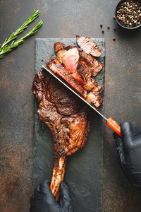 Man in black gloves cuts grilled marble beef steak Tomahawk  Top view  dinner concept