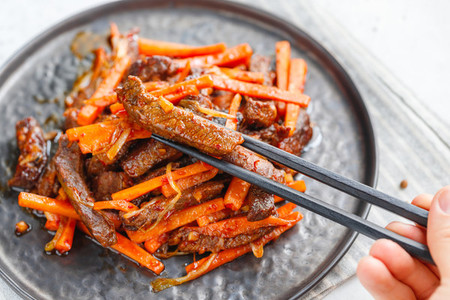 Close up of Chinese spicy Szechuan beef meal on a black plate with wooden sticks over white table