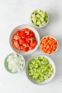 Fresh chopped vegetables in ceramic bowls on a kitchen white table for preparing vegetarian meal  Top view  copy space