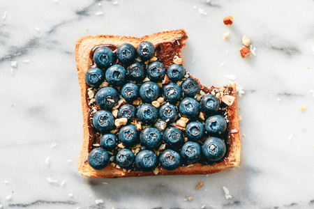 Top view of sweet toast with chocolate spread  blueberries and crashed almond on white marble  Flat lay  breakfast concept