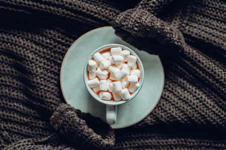 Flat lay of hot chocolate with marshmallow in a ceramic mug over dark green knit winter sweater  The concept of cosy days and Fall  top view