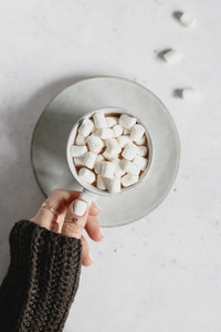 Girls hand holds a cup of hot chocolate with marshmallow over textured white background  Minimalist style  top view  copy space