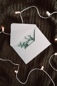 Top view on blank envelope on a warm sweater surrounded festoon lights  Cozy fall or winter flat lay