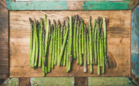 Raw uncooked green asparagus in row over wooden tray background