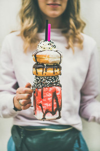 Young woman holding cold strawberry donut freakshake in mason jar