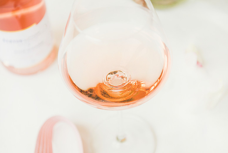 Rose wine in glass and bottle, pink ribbon, peony flowers