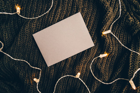 Top view on blank envelope on a warm sweater surrounded festoon lights Cozy fall or winter flat lay