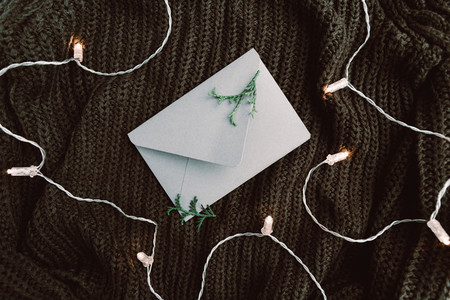Top view on blank envelope on a warm sweater surrounded festoon lights  Cozy fall or winter flat lay