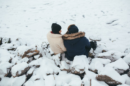 man and woman sitting on the snow covered rocks