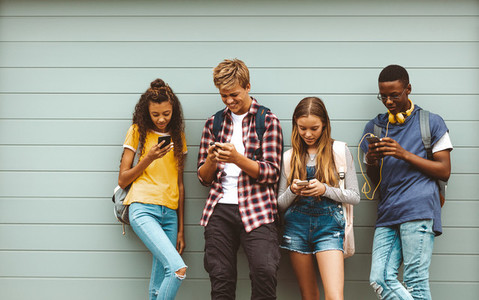 Teenage boys and girls using cell phones standing outdoors