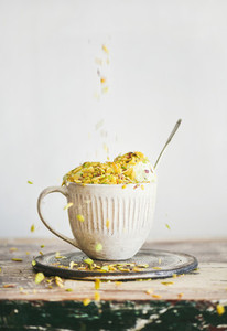 Pistachio ice cream in mug with nuts falling from above