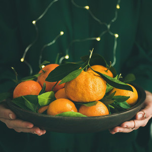 Fresh tangerine fruit in plate in female hands square crop