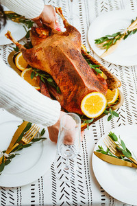 Woman sets a golden tray with whole roasted goose on a festive table   Thanksgiving or Christmas family dinner