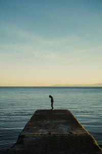 Boy in hoody standing on ocean pier 01