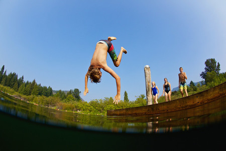 Boy somersaulting off dock into sunny summer lake 01