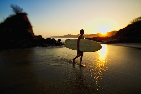 Silhouette boy with surfboard walking on idyllic ocean beach 01
