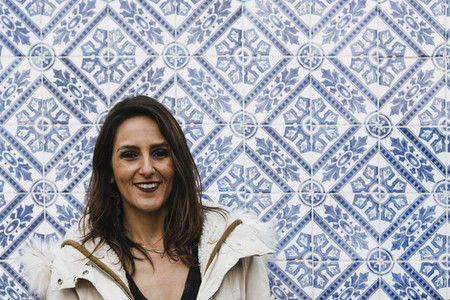 Portrait happy woman standing against blue and white mosaic wall 01