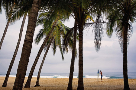 Male surfer with surfboard on tropical beach with palm trees 01