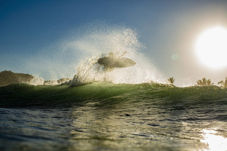 Surfer catching air behind ocean wave at sunrise 01