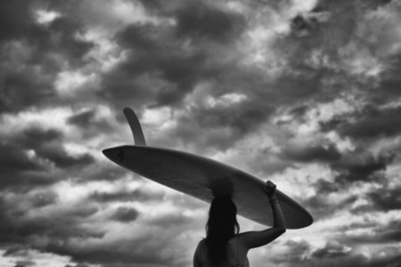 Female surfer carrying long board overhead under cloudy sky 01