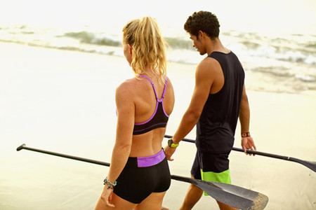 Young fit couple with oars walking on beach 01
