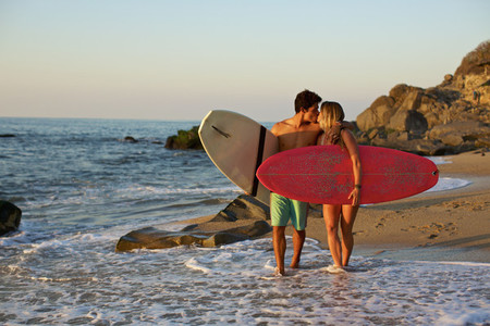 Young affectionate couple with surfboards walking on sunny ocean beach 02